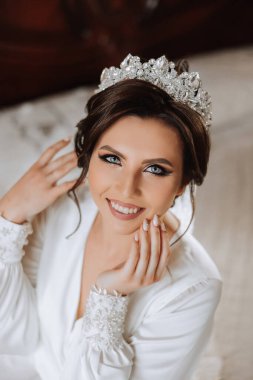 Saçında taç olan güzel bir esmer gelin güzel bir bornozla düğün için hazırlanıyor. Yakın plan düğün fotoğrafı, fotoğraf..