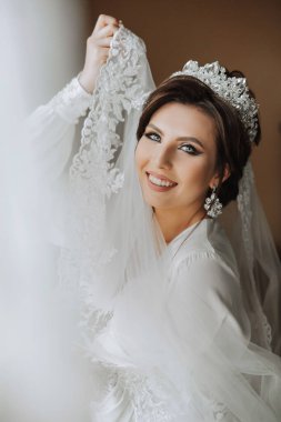 Saçında taç olan güzel bir esmer gelin güzel bir bornozla düğün için hazırlanıyor. Yakın plan düğün fotoğrafı, fotoğraf..