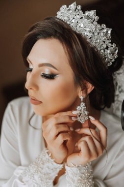 Saçında taç olan güzel bir esmer gelin güzel bir bornozla düğün için hazırlanıyor. Yakın plan düğün fotoğrafı, fotoğraf..