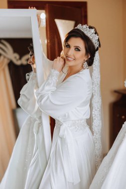 Yansıması olan bir aynanın yanında, yatak odası tarzı lüks bir gelin portresi. Sabahleyin gelini beyaz bir cübbeyle düğüne hazırlıyorum..