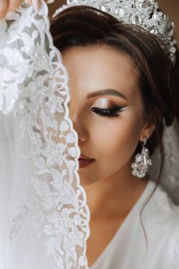 Saçında taç olan güzel bir esmer gelin güzel bir bornozla düğün için hazırlanıyor. Yakın plan düğün fotoğrafı, fotoğraf..