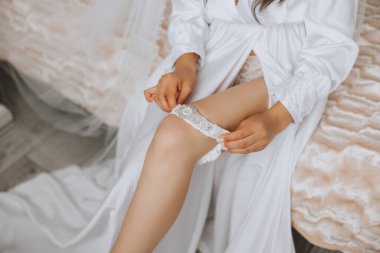 Gelinin düğünden önceki sabahı. Duvağı ve beyaz bornozlu güzel bir saç stili olan güzel bir genç kadın. Gelinliğinin yanında bir mankenin üzerinde. Profesyonel makyaj. Son hazırlıklar.