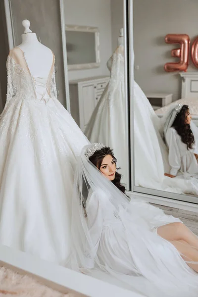 鏡の近くのボードビールスタイルの豪華な花嫁の肖像画 白いローブで朝の結婚式のための花嫁の準備 — ストック写真