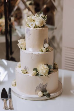 Ziyafet salonunda büyük lüks, çok katmanlı bir düğün pastası taze beyaz gül çiçekleriyle süslenir. Akşam ışığında düğün tatlısı. Düğün dekoru.
