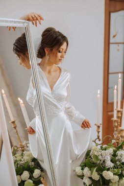 Yansıması olan bir aynanın yanında, yatak odası tarzı lüks bir gelin portresi. Sabahleyin gelini beyaz bir cübbeyle düğüne hazırlıyorum..