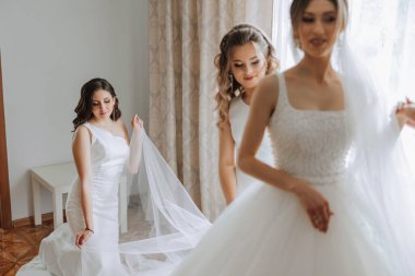 Gelinin sabahı. Gelinin baş nedimesi gelinin elbisesini bağlar, düğmelerini ya da kollarını bağlar. Kız arkadaşlar gelinin elbisesini bağlamasına yardım edin.