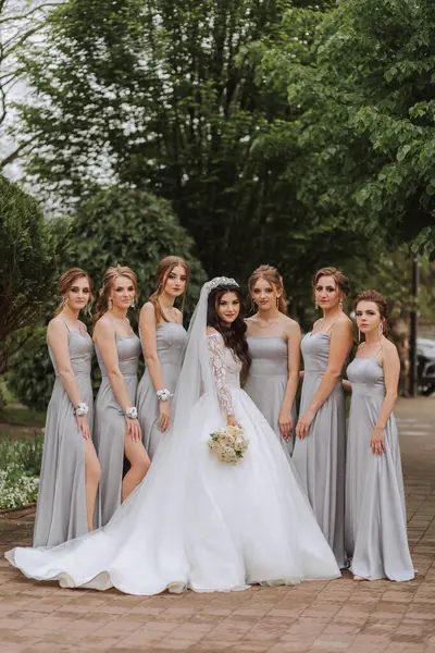 Group portrait of the bride and bridesmaids. A bride in a wedding dress and bridesmaids in silver dresses hold stylish bouquets on their wedding day.
