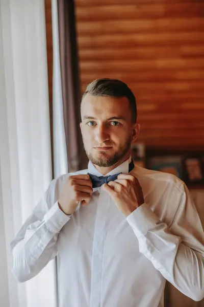 A stylish groom is tying his tie, preparing for the wedding ceremony. Groom\'s morning. A businessman wears a tie. The groom is getting ready in the morning before the wedding ceremony.