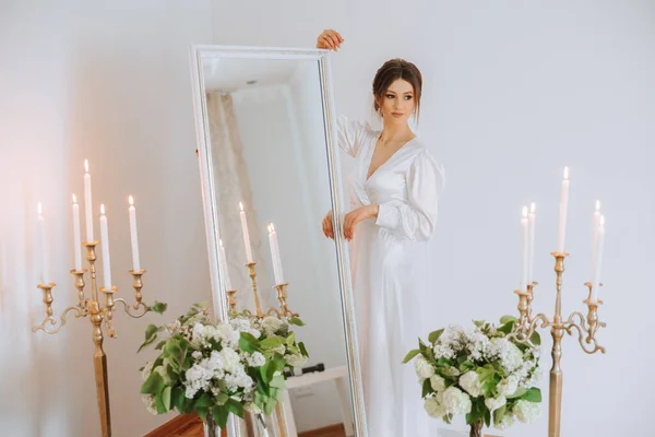 美しいブルネットの花嫁は 新鮮な花とミラーの背景に対するスタイリッシュなキャンドルスティックの間の美しいブードゥールスタイルのドレスで結婚式のために準備しています 結婚式の肖像画 — ストック写真