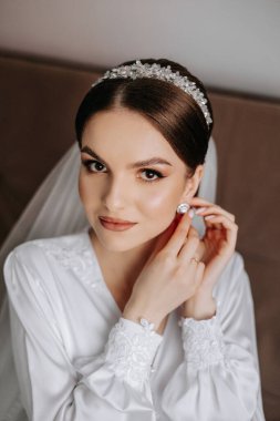 Saçında taç olan güzel bir esmer gelin güzel bir bornozla düğün için hazırlanıyor. Yakın plan düğün fotoğrafı, fotoğraf..