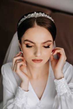 Saçında taç olan güzel bir esmer gelin güzel bir bornozla düğün için hazırlanıyor. Yakın plan düğün fotoğrafı, fotoğraf..