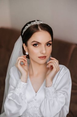 Saçında taç olan güzel bir esmer gelin güzel bir bornozla düğün için hazırlanıyor. Yakın plan düğün fotoğrafı, fotoğraf..