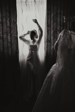 Bir düğün sabahında geceliğiyle pencerenin önünde duran bir kadın. Siyah beyaz fotoğraf.