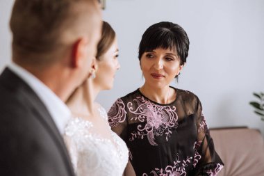 Mutlu ebeveynler evlenen gelinin elini tutuyor ve ona destek oluyor. Gelinlik ve duvak takıyor..