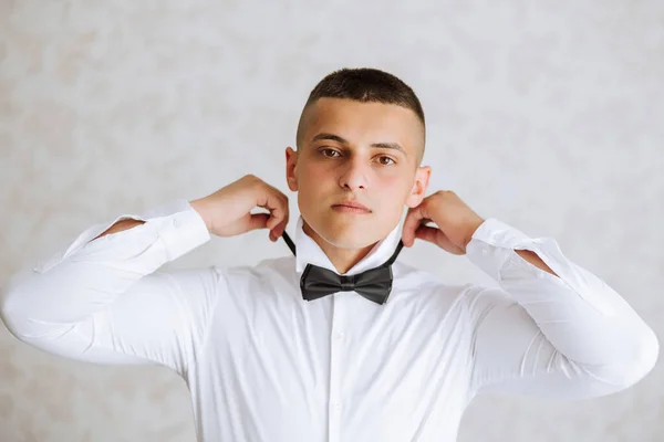 A stylish groom is tying his tie, preparing for the wedding ceremony. Groom\'s morning. A businessman wears a tie. The groom is getting ready in the morning before the wedding ceremony.