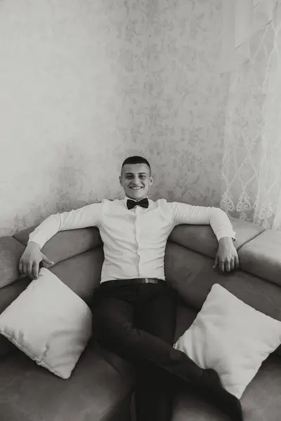 Stylish portrait of the groom preparing for the wedding ceremony. Groom\'s morning. The groom is sitting on the sofa. The confident look of a mature man. Black and white photo.