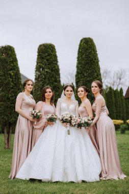 Gelin ve nedimelerin toplu portresi. Gelinlik giymiş bir gelin, pembe ya da tozlu elbiseler giymiş nedimeler ve düğün günü şık buketler tutan gelinlikler..