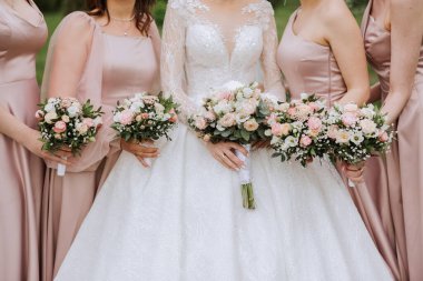 Gelin ve nedimelerin toplu portresi. Gelinlik giymiş bir gelin, pembe ya da tozlu elbiseler giymiş nedimeler ve düğün günü şık buketler tutan gelinlikler..