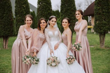 Gelin ve nedimelerin toplu portresi. Gelinlik giymiş bir gelin, pembe ya da tozlu elbiseler giymiş nedimeler ve düğün günü şık buketler tutan gelinlikler..