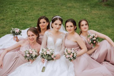 Gelin ve nedimelerin toplu portresi. Gelinlik giymiş bir gelin, pembe ya da tozlu elbiseler giymiş nedimeler ve düğün günü şık buketler tutan gelinlikler..