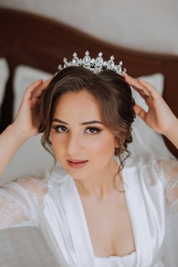 Saçında taç olan güzel bir esmer gelin güzel bir bornozla düğün için hazırlanıyor. Yakın plan düğün fotoğrafı, fotoğraf..