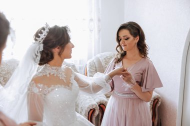 Gelinin sabahı. Gelinin baş nedimesi gelinin elbisesini bağlar, düğmelerini ya da kollarını bağlar. Kız arkadaşlar gelinin elbisesini bağlamasına yardım edin.