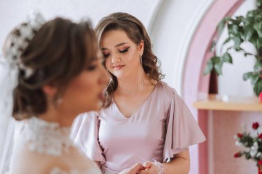 Gelinin sabahı. Gelinin baş nedimesi gelinin elbisesini bağlar, düğmelerini ya da kollarını bağlar. Kız arkadaşlar gelinin elbisesini bağlamasına yardım edin.