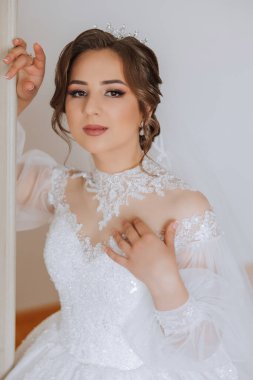 Şık bir gelinlik içinde siyah saçlı ve düğün sabahı odasında çarpıcı makyajlı güzel bir gelinin moda fotoğrafı. Gelin düğün için hazırlanıyor.