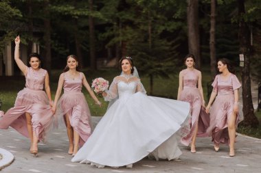 Gelin ve nedimelerin toplu portresi. Gelinlik giymiş bir gelin, pembe ya da tozlu elbiseler giymiş nedimeler ve düğün günü şık buketler tutan gelinlikler..