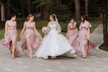 Gelin ve nedimelerin toplu portresi. Gelinlik giymiş bir gelin, pembe ya da tozlu elbiseler giymiş nedimeler ve düğün günü şık buketler tutan gelinlikler..