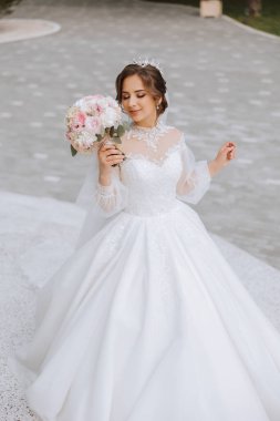 Omzundan ayrılmış esmer gelin dantelli beyaz elbise ve bir buket beyaz ve pembe çiçekle poz veren taç. Güzel saç ve makyaj. Bahar düğünü