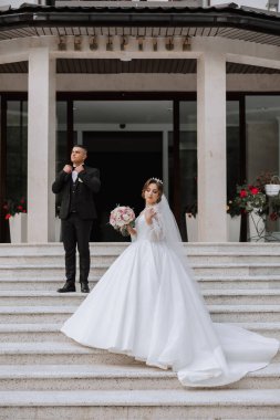 Büyük, güzel bir merdivende klasik gelinlik içinde yeni evlilerin portresi. Gelin ve damat için mağaza ve mal satışı kavramı.