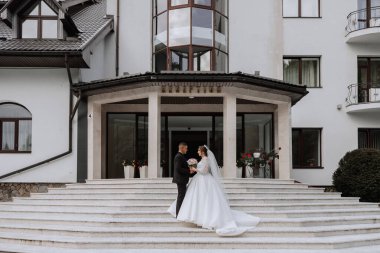 Büyük, güzel bir merdivende klasik gelinlik içinde yeni evlilerin portresi. Gelin ve damat için mağaza ve mal satışı kavramı.