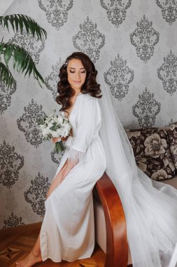 Saçında taç olan güzel bir esmer gelin güzel bir bornozla düğün için hazırlanıyor. Düğün portresi, fotoğraf.