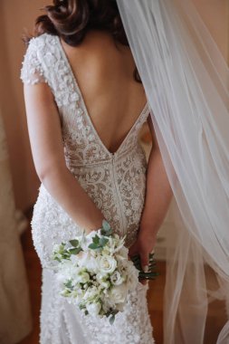 Dar gelinlikli gelin arkasında bir buket beyaz gül tutuyor. Gelinin güzel detayları.