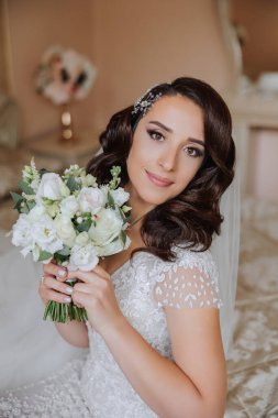 Genç bir gelinin harika bir portresi. Uzun kıvırcık saçlı, düğün makyajı ve mücevher çelengi olan güzel bir gelin. İçi güzel kahverengi gözlü bir düğün fotoğrafı modeli..