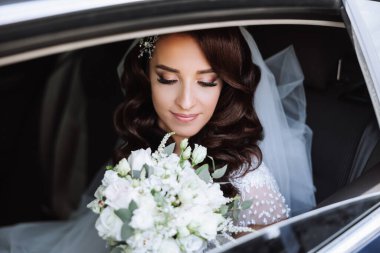 Arabada oturan güzel bir gelin, arabanın açık penceresinden dışarı bakar. Elinde bir buket çiçekle güzel bir gelin şık ve pahalı bir arabada oturuyor..