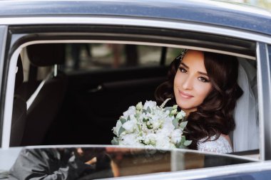 Arabada oturan güzel bir gelin, arabanın açık penceresinden dışarı bakar. Elinde bir buket çiçekle güzel bir gelin şık ve pahalı bir arabada oturuyor..