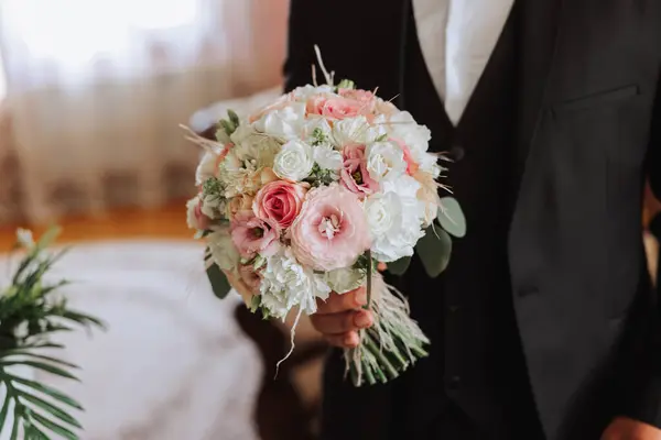 Stylish portrait of the groom with a bouquet of flowers. A man is preparing for a wedding ceremony in the morning. Groom\'s morning. Preparation for the groom\'s morning. Young and handsome groom.