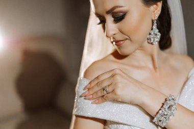 Otel odasında gelinin portresi. Güzel genç bir kız beyaz bir gelinlik giyiyor. Modern düğün saç stili. Doğal makyaj..