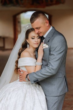 Yakışıklı bir damat, gelinini bembeyaz bir elbiseyle kucaklıyor ve güzel bir açık havada gülümsüyor. Açık gökyüzünün altında. Yüksek kalite fotoğraf. Yeni evli bir çift güneşli bir yaz gününde birlikte poz verir..