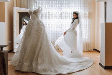 Odasında uzun peçeli, bornoz giymiş güzel bir gelin. Bir mankenin üzerinde gelinlik. Düğün töreninden önceki sabah gelin..