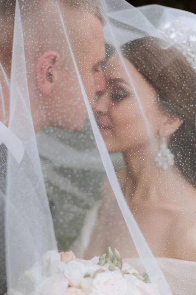 Close-up portrait of two people in love. An affectionate groom embraces the bride, supporting her under the veil. The best moments of the wedding.