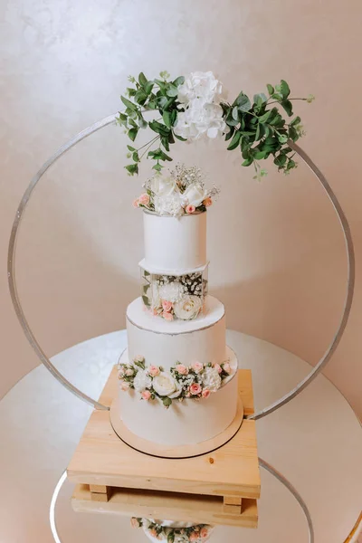 a three-tiered wedding cake decorated with flowers stands on a mirrored table. Decorative wedding cake. Beauty is in the details.