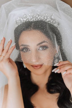 Beyaz gelinlik içinde duvak tutan genç bir gelin otel odasında esmer gelin portresi, düğünden önceki sabah..