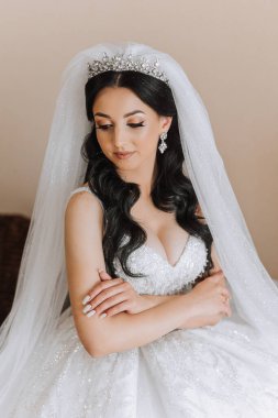 Otel odasında gelinin portresi. Güzel genç bir kız beyaz bir gelinlik giyiyor. Modern düğün saç stili. Doğal makyaj..