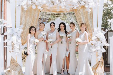 Çiçeklerle süslenmiş bir kemerin yanında aynı elbiseli güzel kızlar. Yaz fotoğrafı.