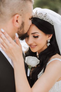 Damat, bir yaz günü gelinini tapınakta güzel bir doğanın arka planına karşı öper. - Sanat. Seçici odak.