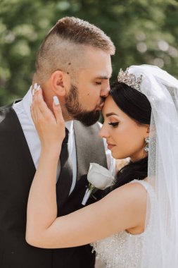 Damat, bir yaz günü gelinini tapınakta güzel bir doğanın arka planına karşı öper. - Sanat. Seçici odak.