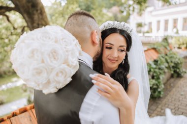 Damat, bir yaz günü gelinini tapınakta güzel bir doğanın arka planına karşı öper. - Sanat. Seçici odak.